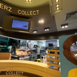 Widok na ladę strefy „Collect” w restauracji McDonald's z włączonym ekranem zamówień i kuchnią w tle.