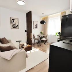 Jasny, nowoczesny salon z aneksem kuchennym i czarną zabudową.